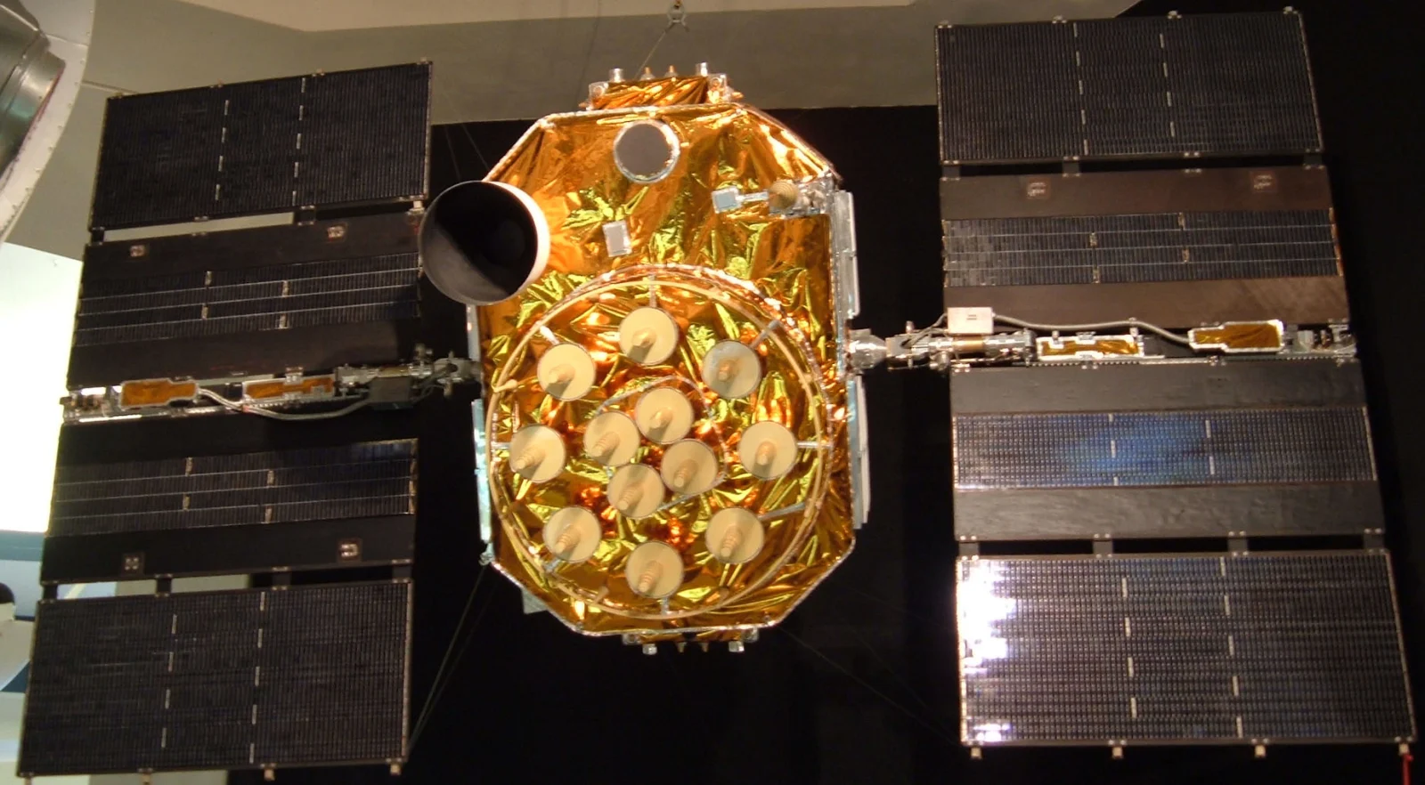 Frontansicht eines ausgestellten GPS-Block-IIA-Satelliten mit goldfarbenem Körper, Antennenfeld und ausgeklappten Solarpaneelen